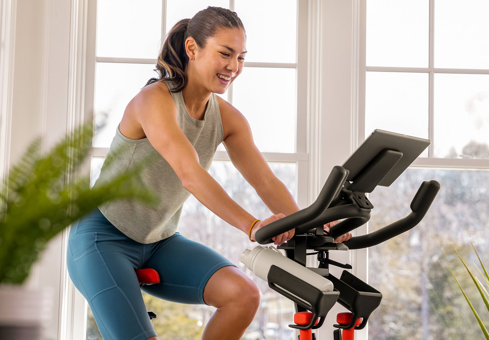 Woman riding the BowFlex C6 Bike and smiling at a tablet on the bike's media shelf.