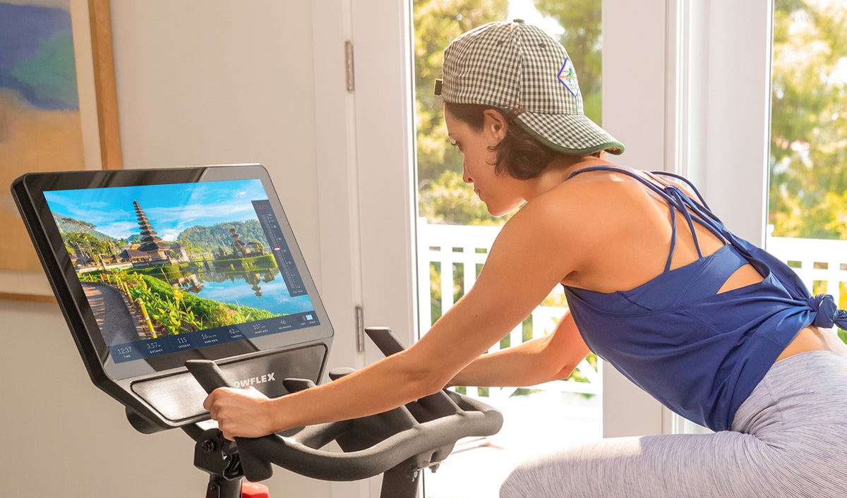 Woman exercising on the BowFlex VeloCore Bike 22 and looking at its touchscreen.