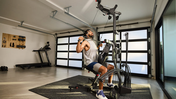 Man using the steel curved lat bar on the BowFlex Xtreme 2 SE in a home gym.