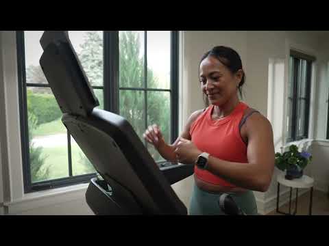 A woman smiling while exercising on the BowFlex T9 Treadmill inside a bright, modern room.