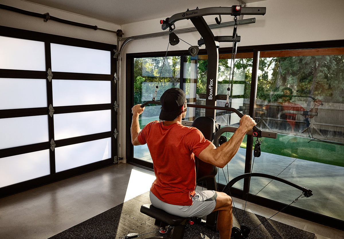 A man seated on and facing the BowFlex Xtreme 2 SE using its angled lat bar to workout in a home gym.