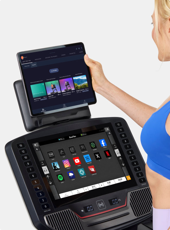 Woman interacting with tablet placed on the BowFlex T16 Treadmill media shelf.