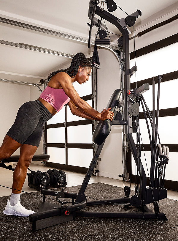 Woman using the cable pulley system on the BowFlex Xtreme 2 SE to do a leg workout in a home gym.