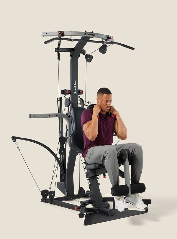 Man seated on the BowFlex Xtreme 2 SE Home Gym, holding onto its cable pulleys while working out.