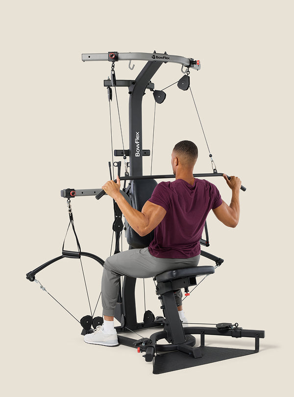 Man seated on and facing the BowFlex Xtreme 2 SE Home Gym, using the angled lat bar to workout.