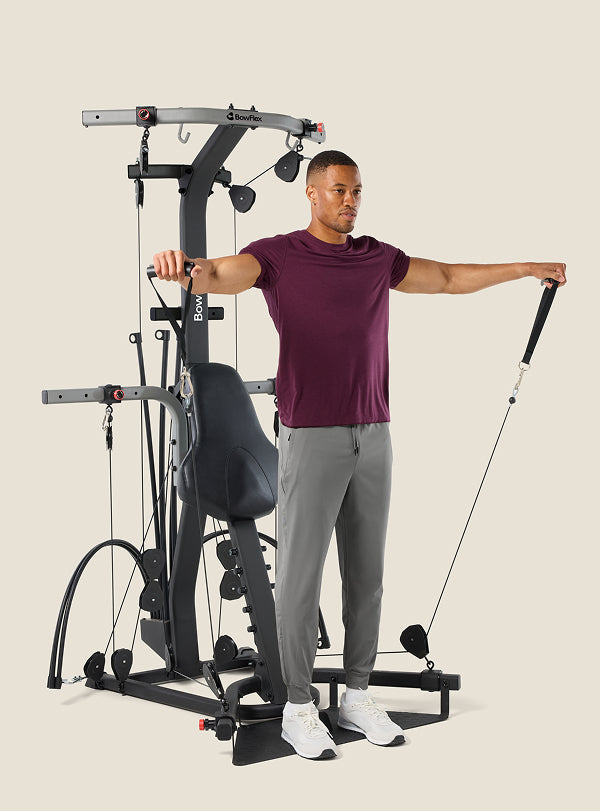 Man standing in front of the BowFlex Xtreme 2 SE Home Gym, holding the cable pulleys with his arms out to his sides.