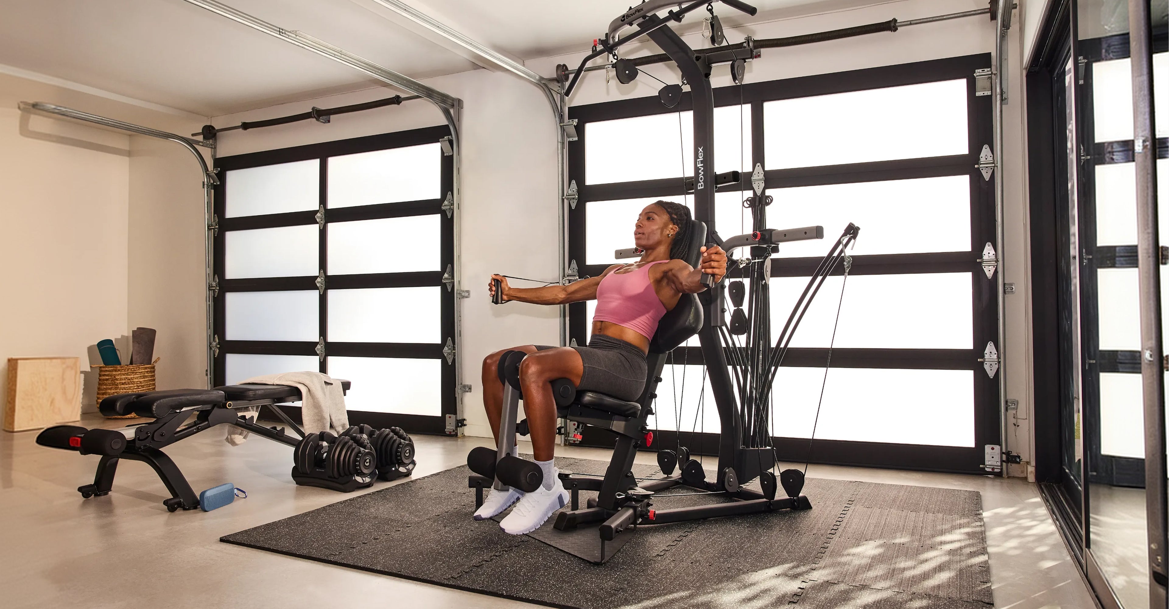 A woman exercises on the X2SE home gym cable machine inside a modern garage with white garage door panels.